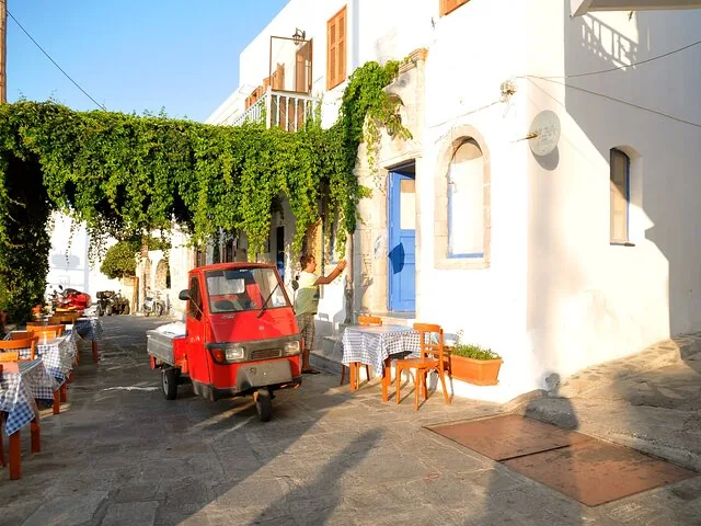A narrow street with a red three-wheeled vehicle and tables