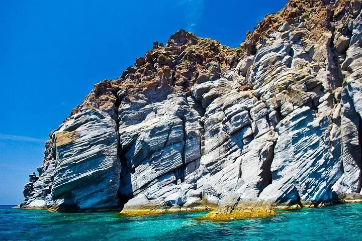 Steep, rugged rock formations rising from the clear blue sea